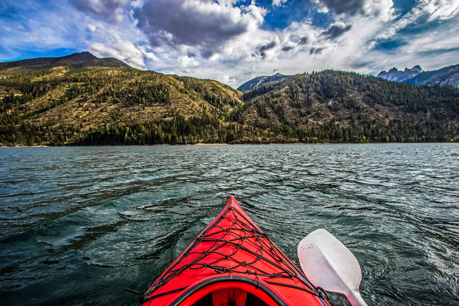 red kayak on body of water near green mountains during daytime
