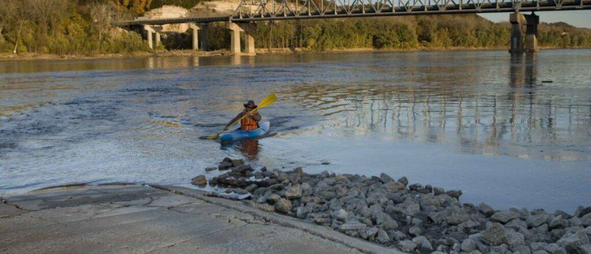 Paddler wearing orange life vest launching kayak at boat ramp