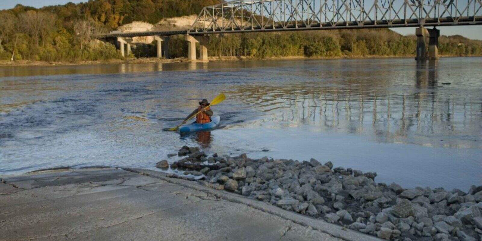 Paddler wearing orange life vest launching kayak at boat ramp